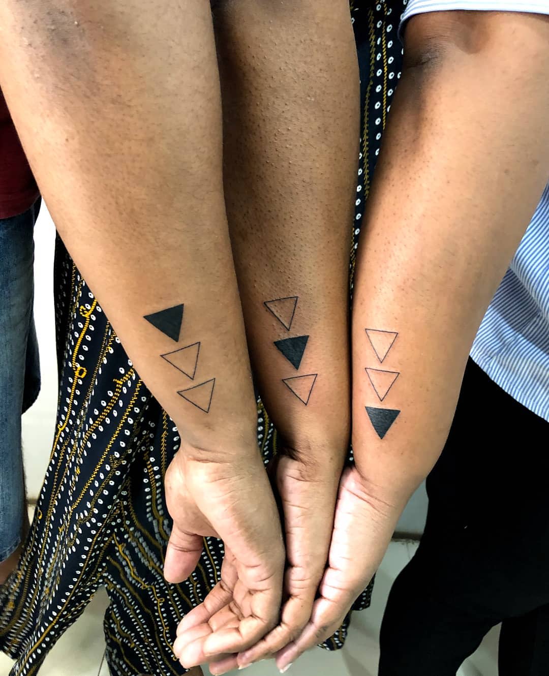 Three arms with triangle tattoos; each arm has one solid triangle